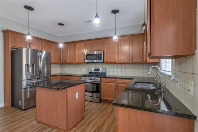 kitchen featuring hanging light fixtures, a kitchen island, sink, dark stone counters, and appliances with stainless steel finishes