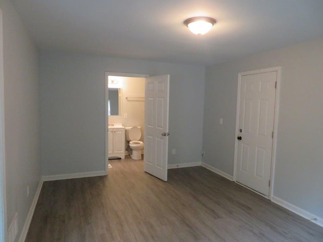 unfurnished bedroom featuring ensuite bathroom, a closet, and hardwood / wood-style flooring