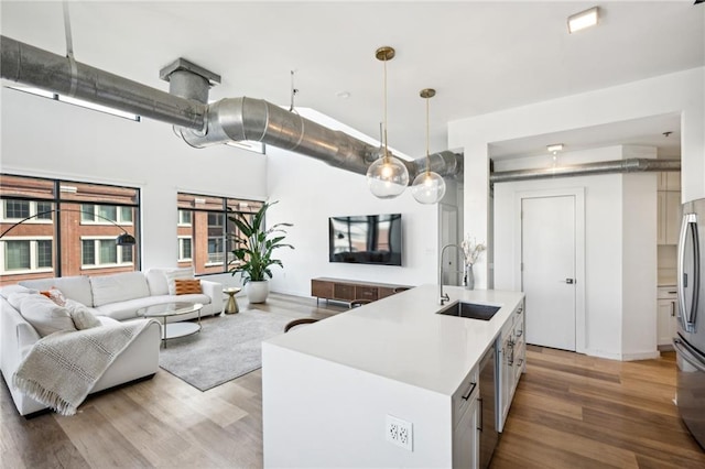 kitchen with appliances with stainless steel finishes, white cabinetry, an island with sink, sink, and hanging light fixtures