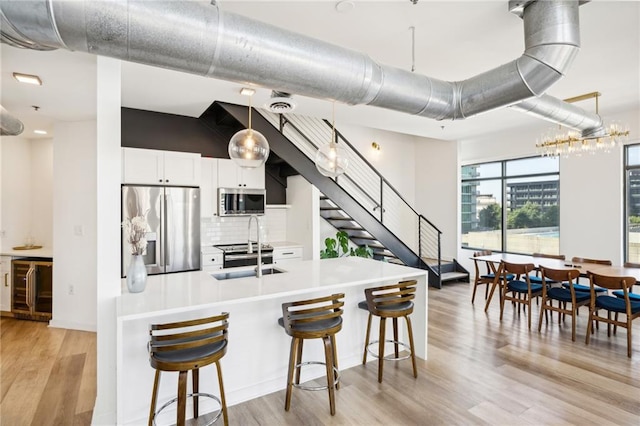 kitchen featuring white cabinetry, appliances with stainless steel finishes, light wood-type flooring, wine cooler, and sink