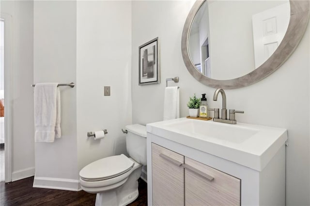 half bath featuring vanity, wood finished floors, toilet, and baseboards