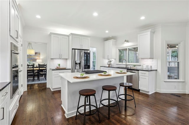 kitchen featuring dark wood finished floors, a kitchen breakfast bar, a center island, stainless steel appliances, and a sink