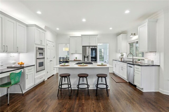 kitchen with a kitchen island, a breakfast bar, dark wood-type flooring, stainless steel appliances, and a sink