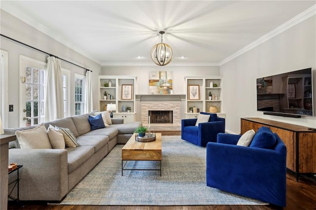 living area featuring a notable chandelier, a fireplace, wood finished floors, and crown molding