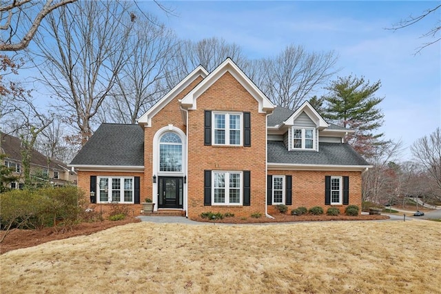 traditional home featuring a front yard, brick siding, and roof with shingles