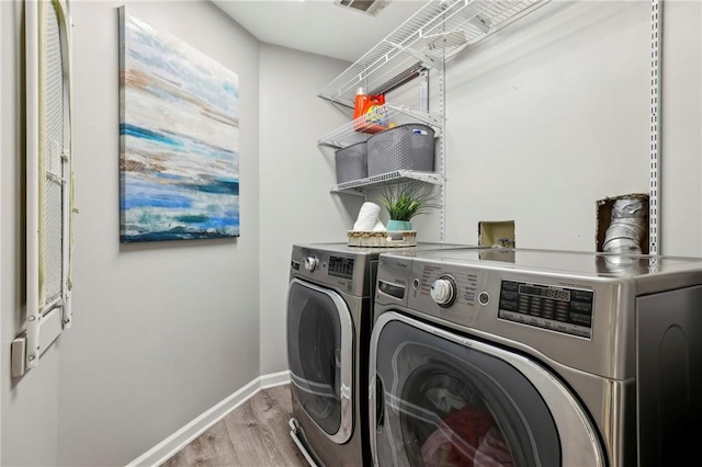 clothes washing area featuring laundry area, baseboards, wood finished floors, and washing machine and clothes dryer