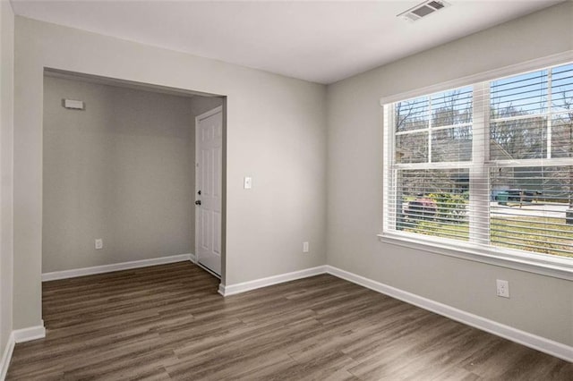 empty room with dark wood finished floors, baseboards, and visible vents