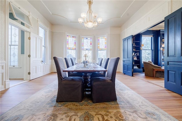 dining room with light wood-style floors, a notable chandelier, a wealth of natural light, and a wainscoted wall