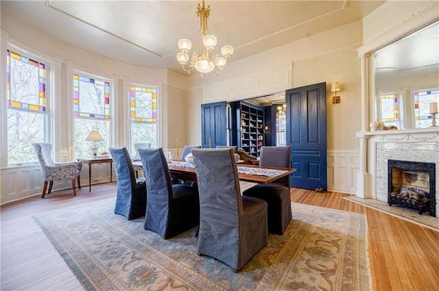 dining room with a decorative wall, an inviting chandelier, a fireplace, a wainscoted wall, and light wood finished floors