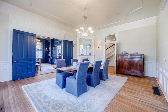 dining room featuring light wood-style floors, a decorative wall, an inviting chandelier, and visible vents