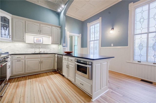 kitchen featuring a peninsula, a wainscoted wall, a sink, stainless steel appliances, and an ornate ceiling