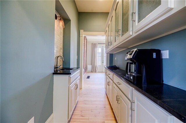 kitchen with glass insert cabinets, a sink, light wood-type flooring, dark countertops, and white cabinetry