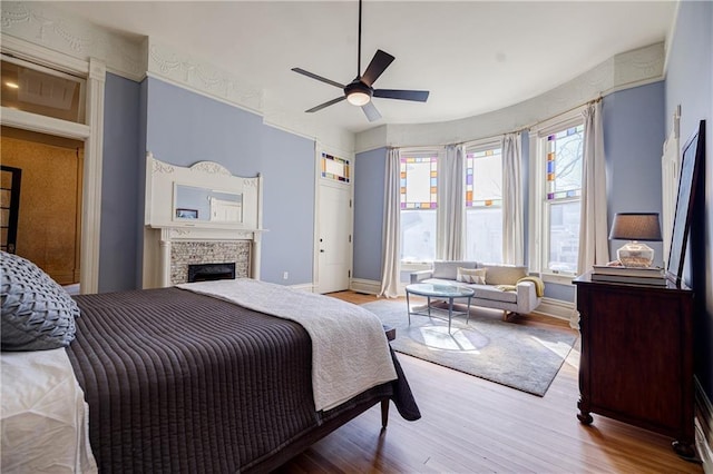 bedroom featuring baseboards, wood finished floors, a brick fireplace, and a ceiling fan