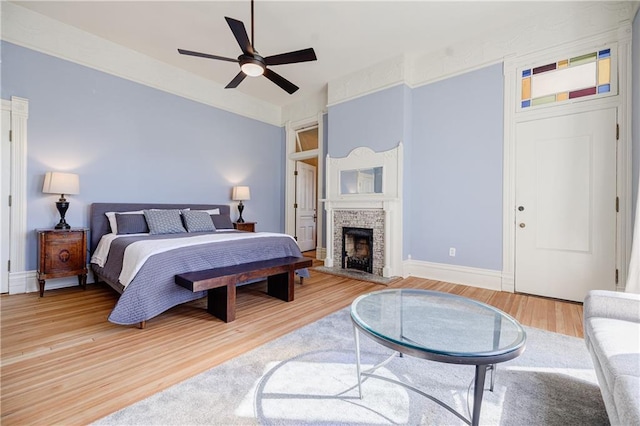 bedroom with light wood finished floors, a fireplace with raised hearth, baseboards, and ceiling fan