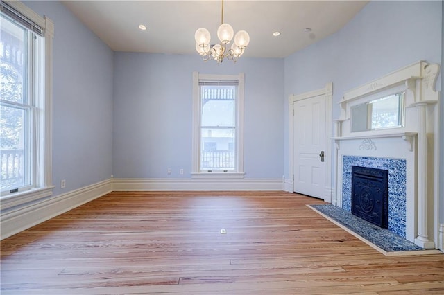 unfurnished living room featuring baseboards, an inviting chandelier, recessed lighting, a fireplace, and light wood-style floors
