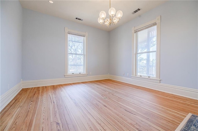 empty room with visible vents, baseboards, light wood-type flooring, and a chandelier