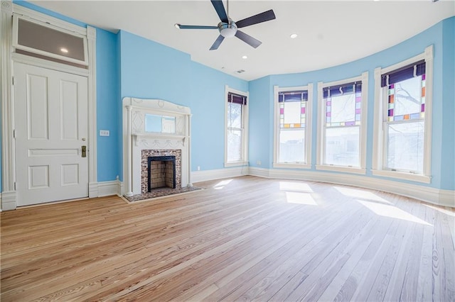 unfurnished living room with a tiled fireplace, ceiling fan, light wood-style floors, and baseboards