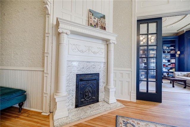 living area featuring a textured wall, a fireplace with flush hearth, wainscoting, and wood finished floors