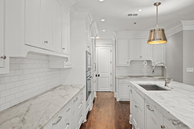 kitchen with sink, hanging light fixtures, appliances with stainless steel finishes, light stone countertops, and white cabinets