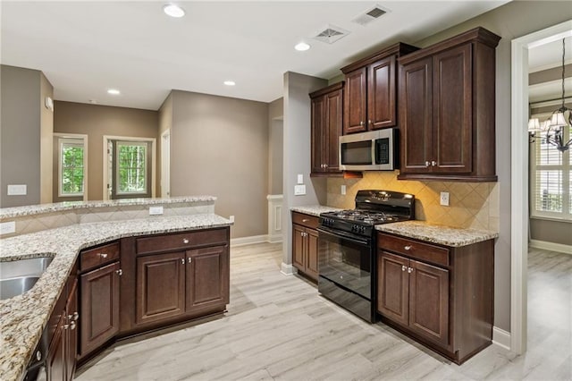 328 Shade Tree Cir, Woodstock, GA 30188 - kitchen with black gas stove, stainless steel microwave, light wood-style flooring, tasteful backsplash, and light stone counters