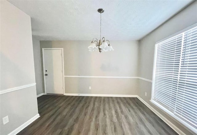 unfurnished dining area with baseboards, a textured ceiling, an inviting chandelier, and wood finished floors