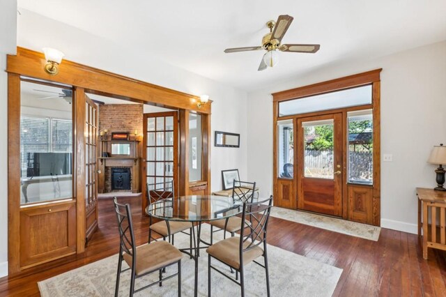 dining room with a brick fireplace, ceiling fan, baseboards, and dark wood finished floors