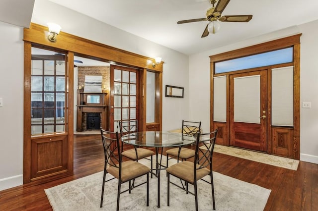 dining space featuring ceiling fan, a brick fireplace, dark hardwood / wood-style flooring, and french doors