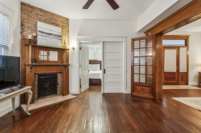 unfurnished living room with a fireplace, dark wood finished floors, baseboards, and ceiling fan