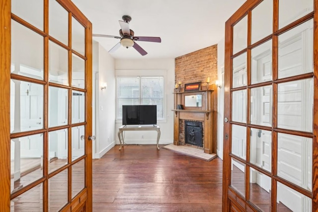 unfurnished living room featuring a large fireplace, dark wood-type flooring, a ceiling fan, baseboards, and french doors