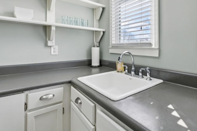 kitchen featuring dark countertops, white cabinetry, a sink, and open shelves