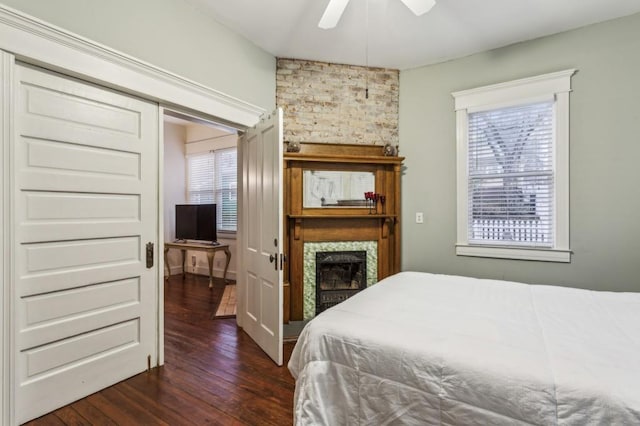 bedroom with a large fireplace, dark wood-style flooring, and a ceiling fan