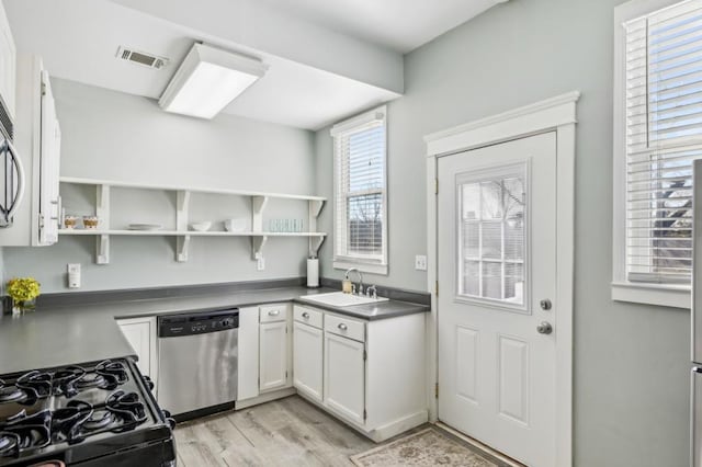 kitchen with open shelves, stainless steel dishwasher, dark countertops, and a sink