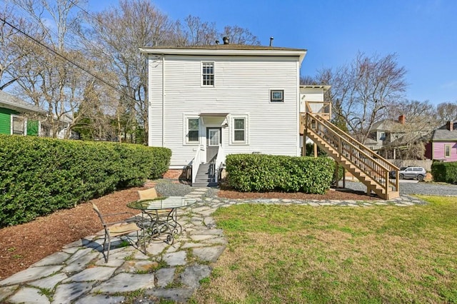 rear view of house featuring entry steps, stairs, and a lawn