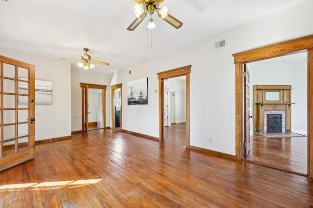 empty room with baseboards, visible vents, a ceiling fan, wood finished floors, and a fireplace