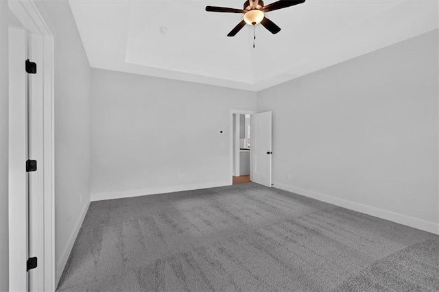 carpeted spare room with ceiling fan, a raised ceiling, and baseboards