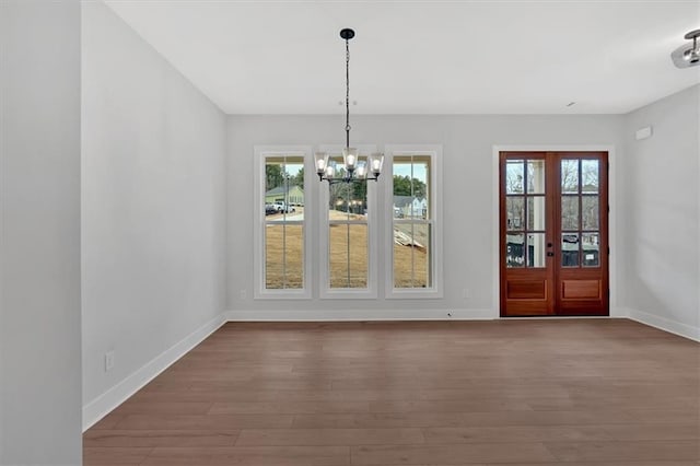 unfurnished dining area featuring a chandelier, baseboards, and wood finished floors