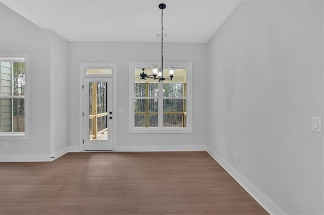 unfurnished dining area with dark wood-style flooring, a notable chandelier, and baseboards