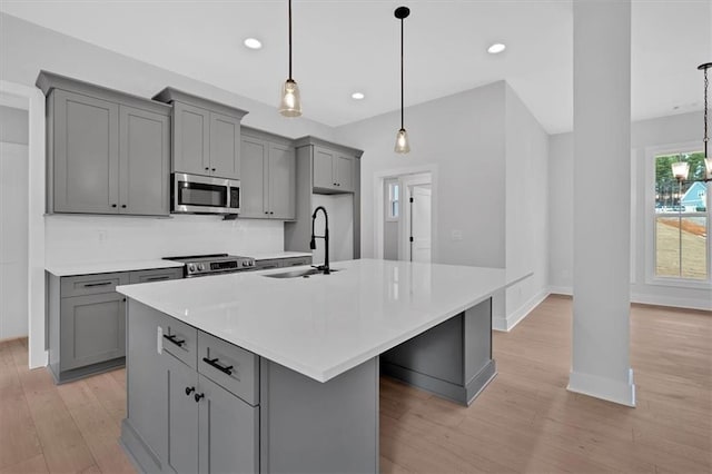 kitchen with light wood finished floors, a sink, gray cabinets, a large island, and appliances with stainless steel finishes