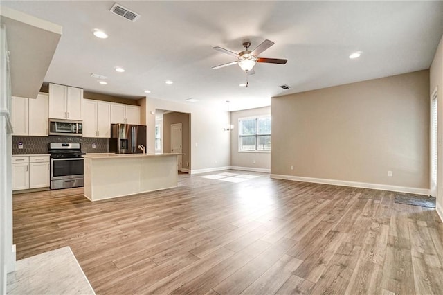 1858 Belmore St SE, Smyrna, GA 30080 - kitchen featuring appliances with stainless steel finishes, open floor plan, a ceiling fan, white cabinets, and tasteful backsplash