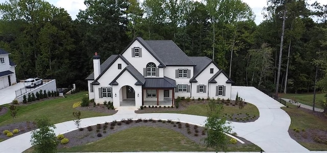 view of front facade with a chimney, metal roof, a standing seam roof, a front yard, and stucco siding