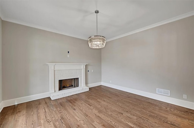 unfurnished living room featuring visible vents, baseboards, wood finished floors, crown molding, and a brick fireplace