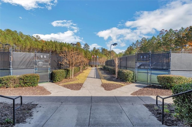 view of community featuring a tennis court, a gate, and fence