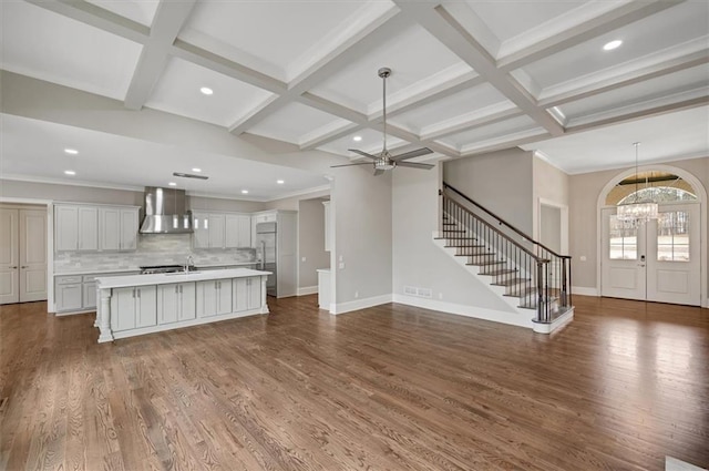 unfurnished living room with beamed ceiling, stairway, coffered ceiling, and wood finished floors