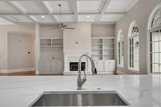 kitchen featuring light stone counters, a fireplace with raised hearth, open floor plan, a sink, and coffered ceiling