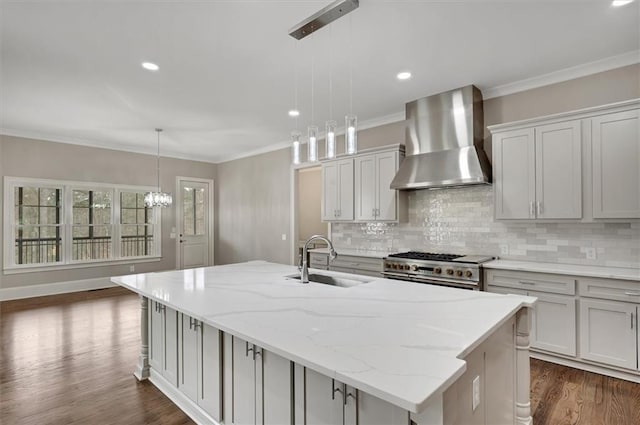 kitchen featuring dark wood-style flooring, a sink, wall chimney range hood, an island with sink, and double oven range