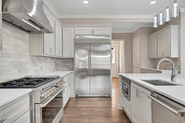 kitchen featuring crown molding, a sink, wall chimney range hood, wood finished floors, and built in appliances