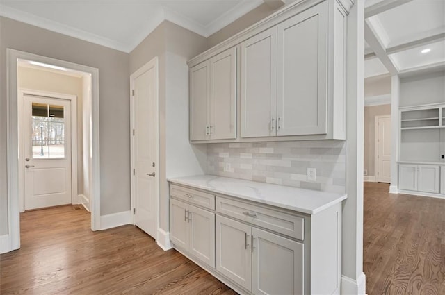 kitchen featuring light stone counters, light wood finished floors, backsplash, ornamental molding, and baseboards