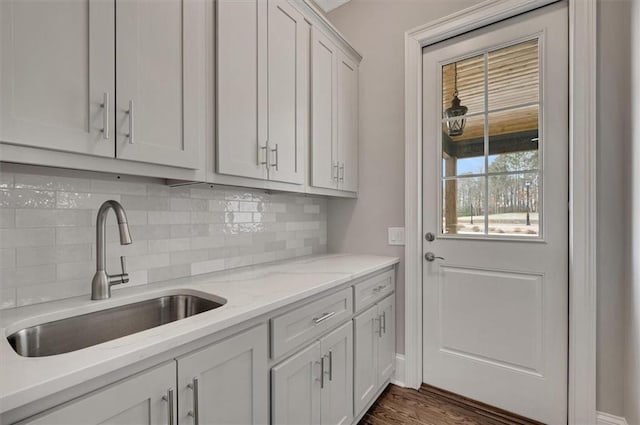 kitchen with a sink, white cabinets, backsplash, light stone countertops, and dark wood finished floors