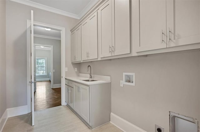 washroom with cabinet space, hookup for a washing machine, crown molding, light wood-type flooring, and a sink