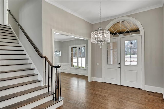 foyer featuring wood finished floors, crown molding, stairway, and an inviting chandelier